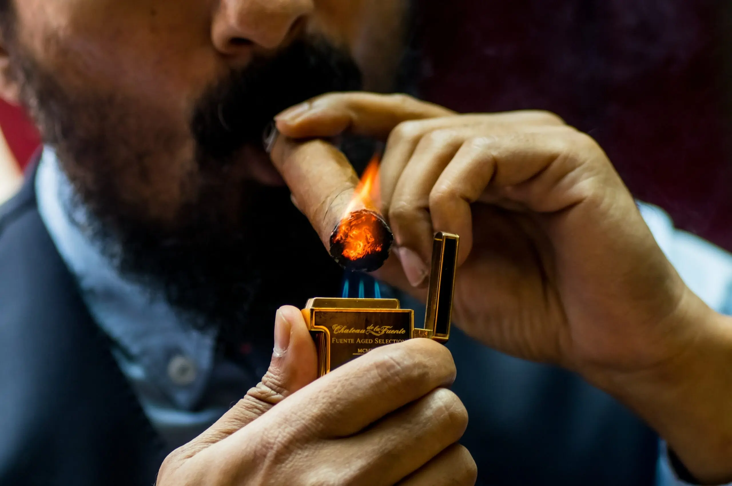 A close-up of a person lighting a cigar, with emphasis on their hands and the glowing tip of the cigar.